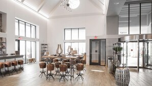 A spacious lobby with high ceilings, large windows, and a central seating area with stools and tables. - Hotel Renovo Des Moines Urbandale,Tapestry Collection Hilton (Urbandale)