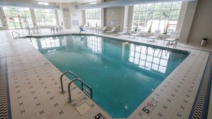 An indoor swimming pool with clear water, tiled floor, and a pool ladder. There are lounge chairs and a windowed wall providing natural light. - Hotel Renovo Des Moines Urbandale,Tapestry Collection Hilton (Urbandale)
