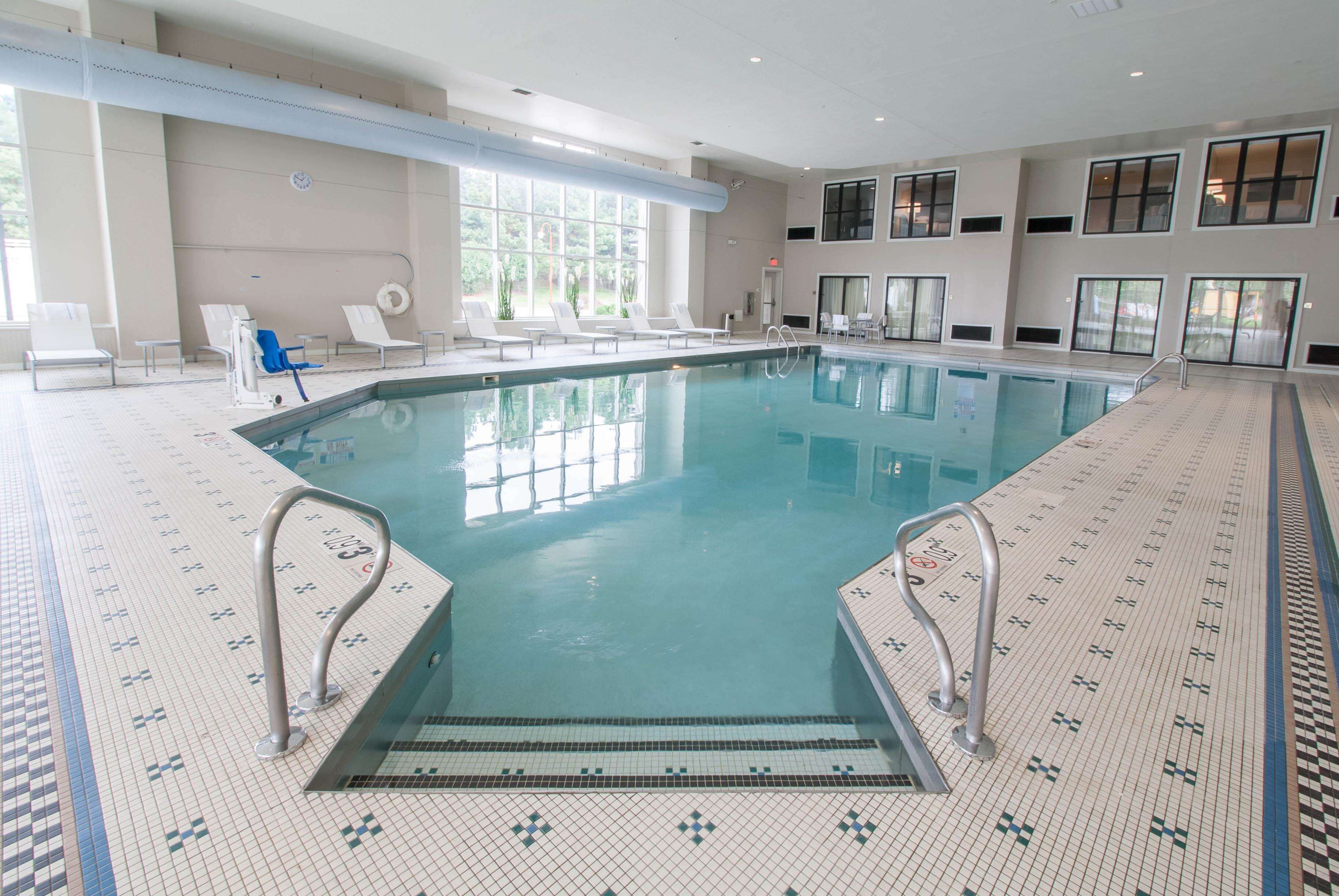 Une piscine intérieure à l’eau claire, dotée d’un sol carrelé et de chaises longues.