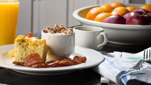 A breakfast setting with a plate of food, a glass of orange juice, and a bowl of fruit. - Hotel Renovo Des Moines Urbandale,Tapestry Collection Hilton (Urbandale)