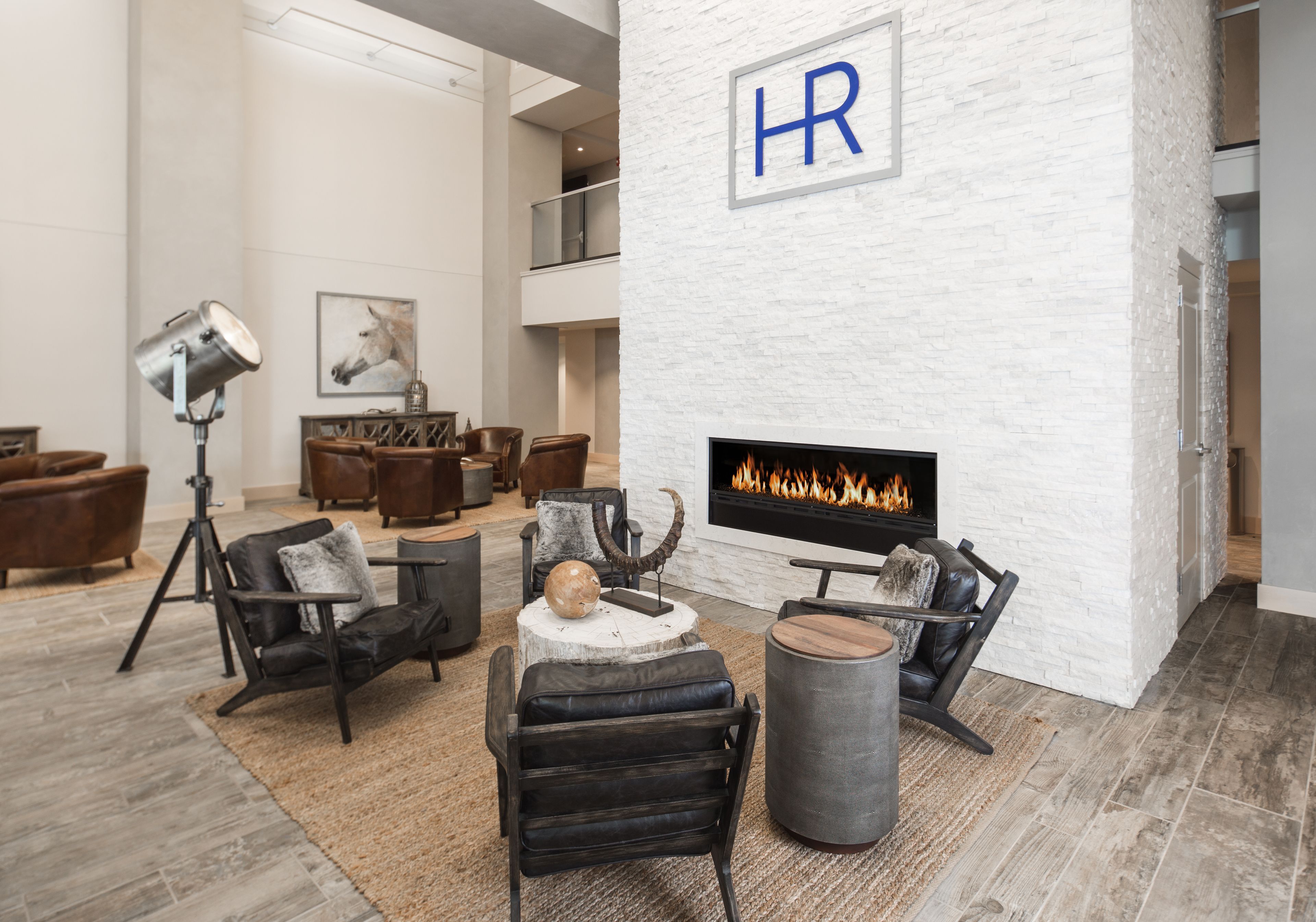 A modern lounge area with leather sofas, a fireplace, and a mounted 'HR' sign on a white brick wall.