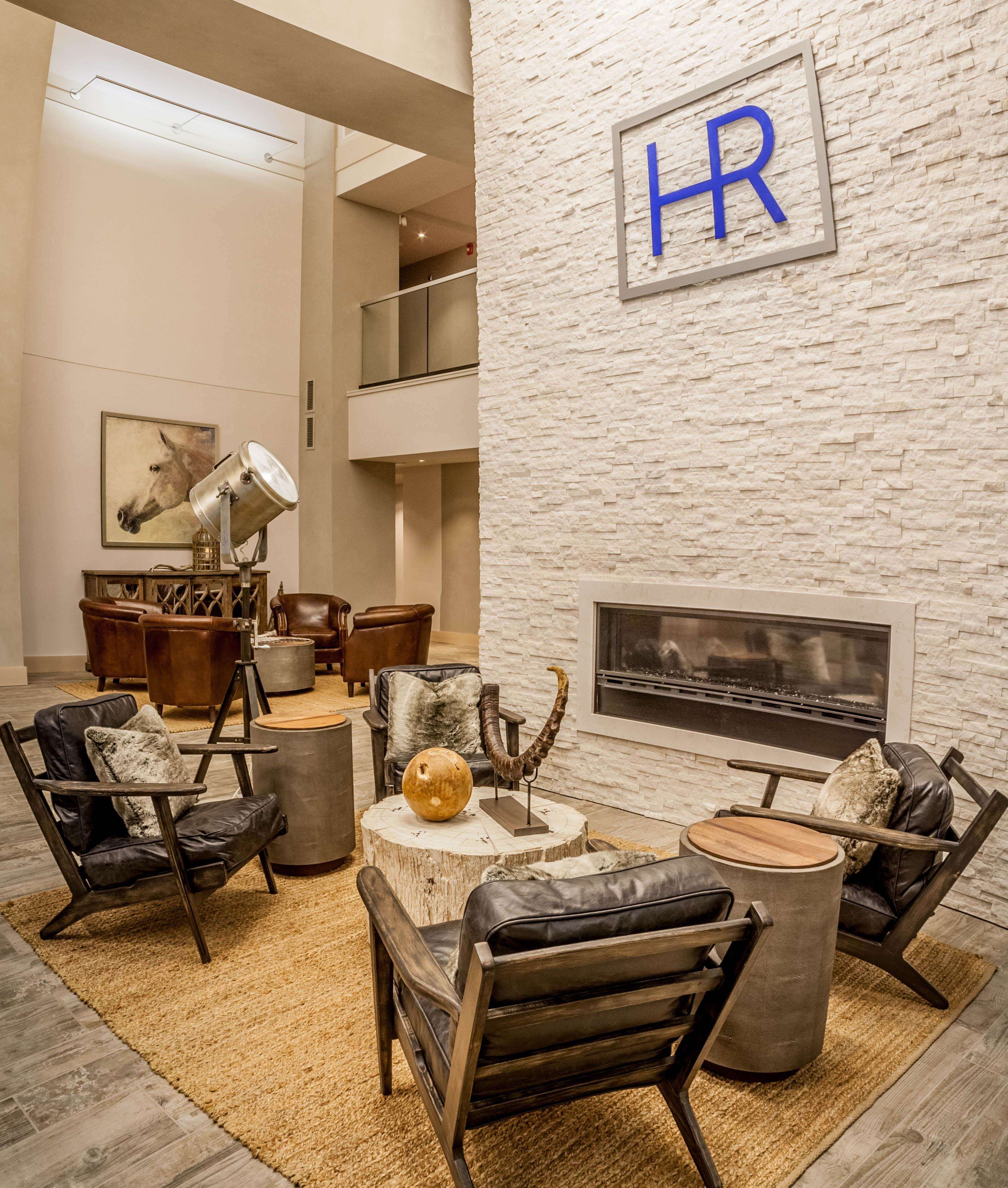 A modern living room with leather sofas, a round coffee table, and a fireplace. A 'HR' sign is mounted on the wall.