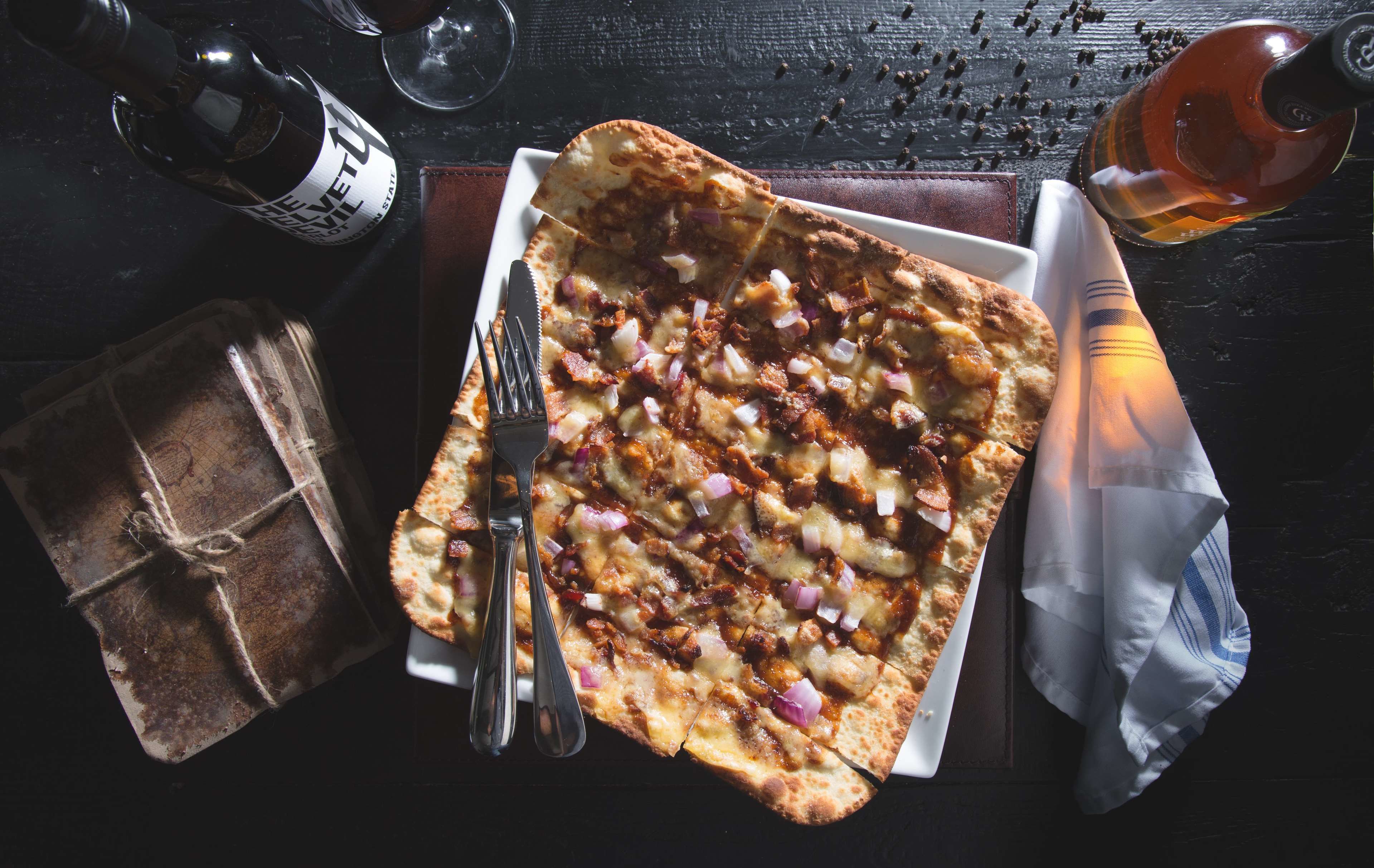 Una pizza con ingredientes, una botella, un vaso y un regalo envuelto sobre una mesa.