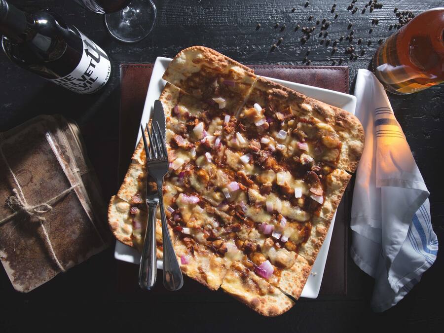 Una pizza con ingredientes, una botella, un vaso y un regalo envuelto sobre una mesa.