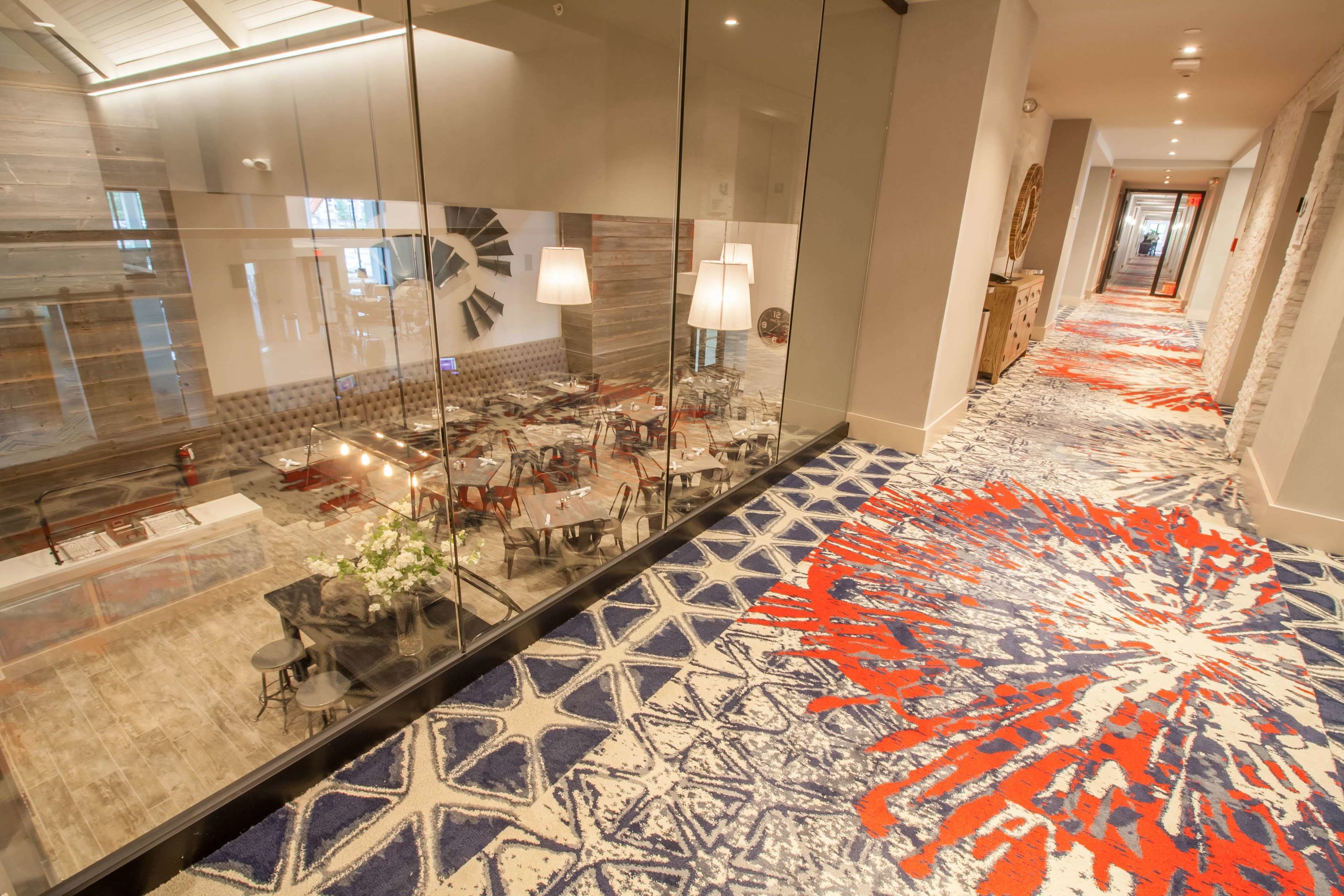 A hotel lobby with a patterned carpet, glass walls, and a seating area with tables and chairs.