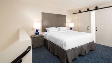 Una habitación de hotel con cama, mesitas de noche, lámparas, un armario y una alfombra azul.