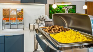 A buffet area with various food options, including sausages and yellow rice, in a modern kitchen setting with stainless steel appliances and a decorative wall. - Comfort Inn Guelph (Guelph)