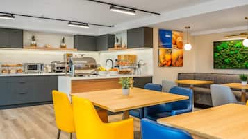 A modern kitchen with grey cabinets, a central island, and a dining area with yellow and blue chairs.