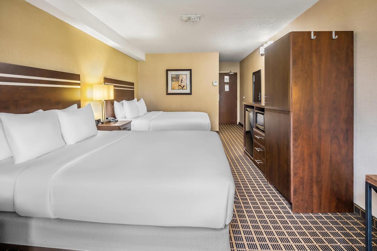 A hotel room with two beds, a desk with a lamp, a wardrobe, and a framed picture on the wall.