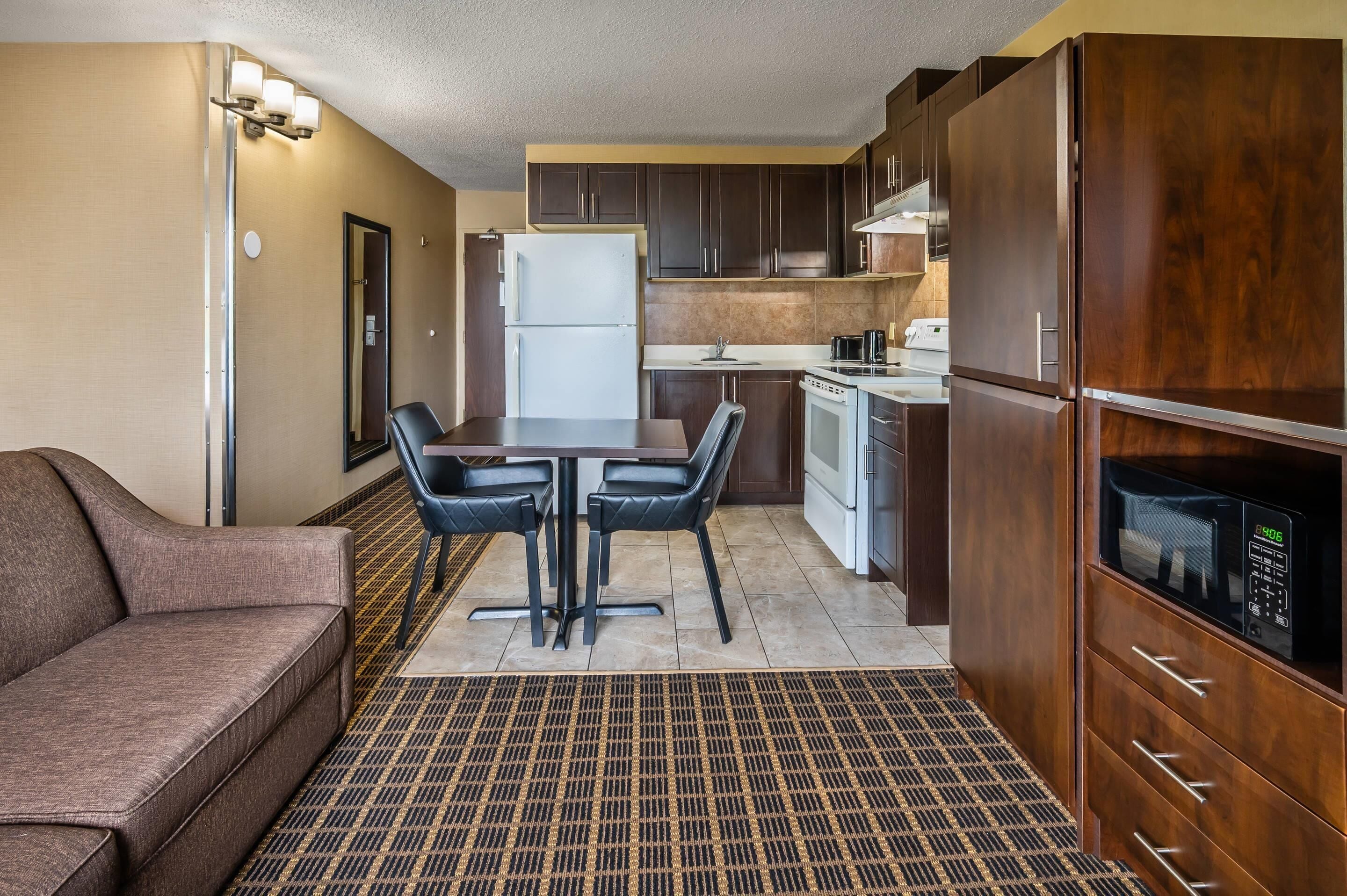 A compact kitchen with a refrigerator, microwave, and stove. There is a dining table with chairs and a sofa in the living area.