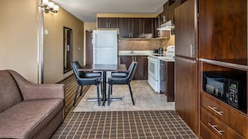 A compact kitchen with a refrigerator, microwave, and stove. There is a dining table with chairs and a sofa in the living area.