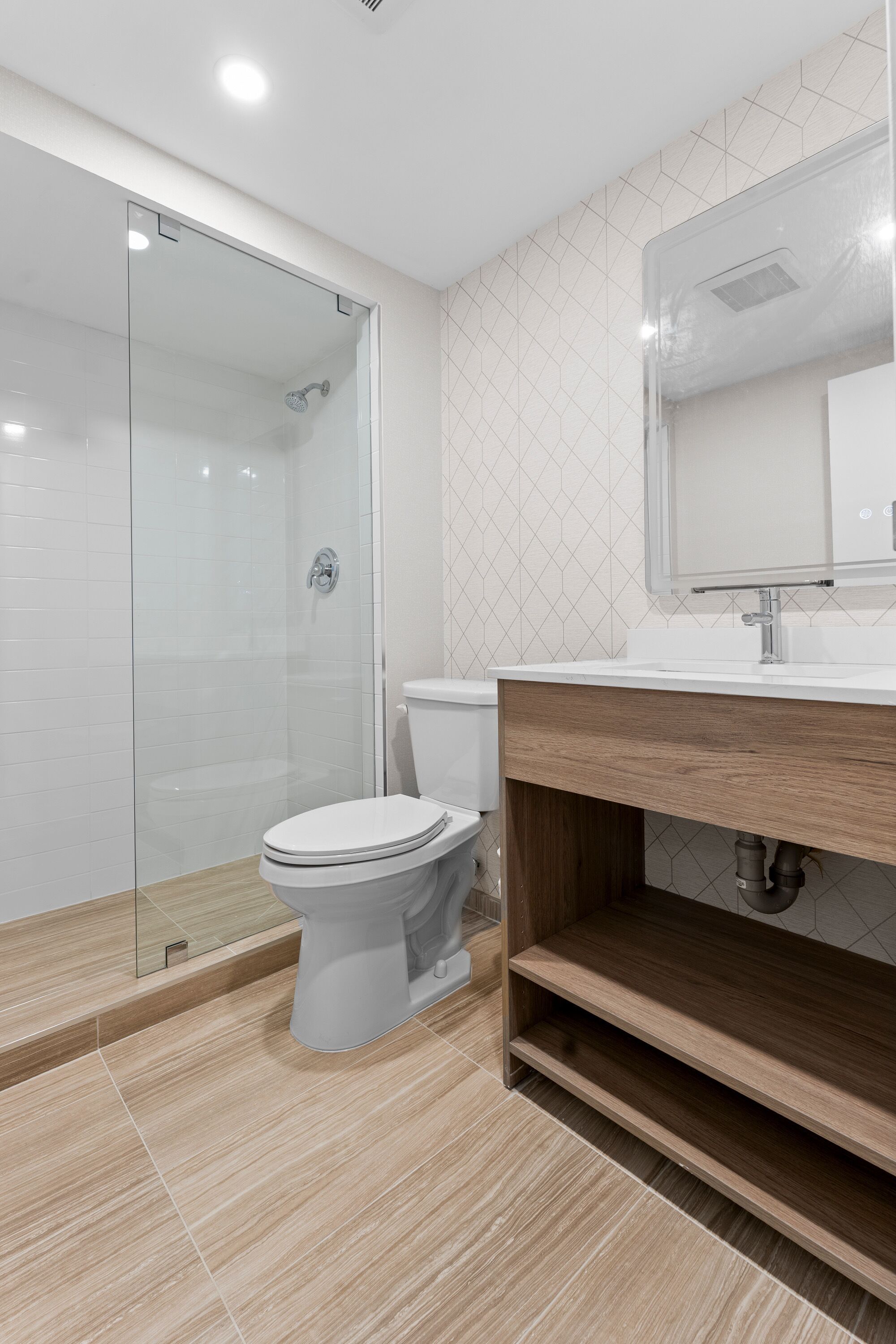 Un baño moderno con cabina de ducha de vidrio, inodoro blanco y tocador de madera con espejo.