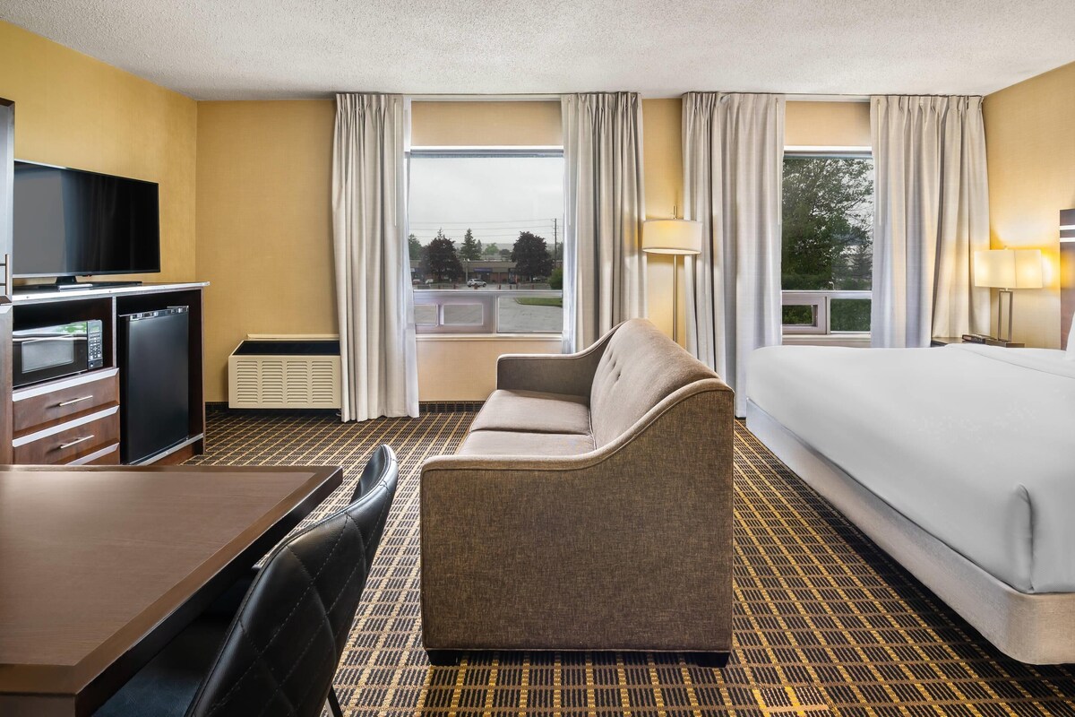 A hotel room with a bed, a sofa, a desk with a TV, and a window with curtains.