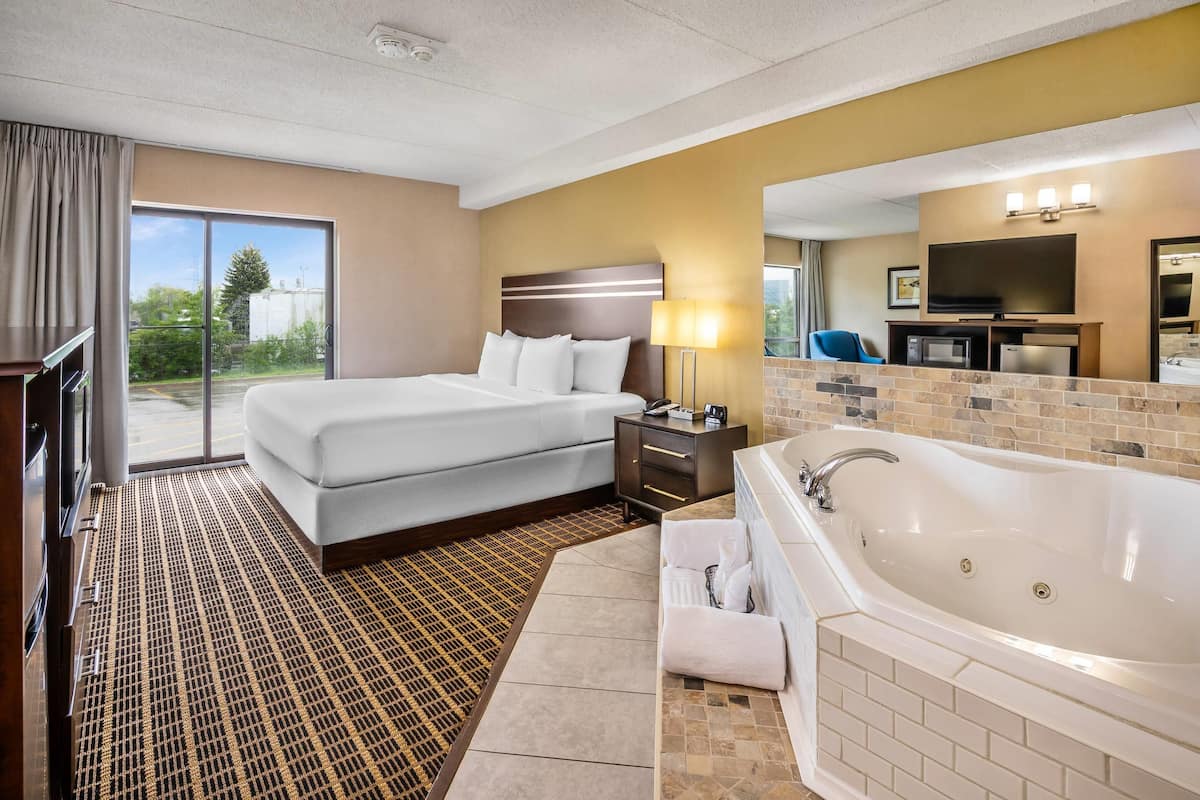 A hotel room with a large bed, a separate sofa, a bathroom with a bathtub, and a TV in the corner.