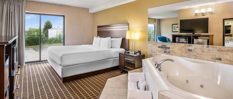 Habitación de hotel con una cama grande, un sofá independiente, baño con bañera y un televisor en la esquina.