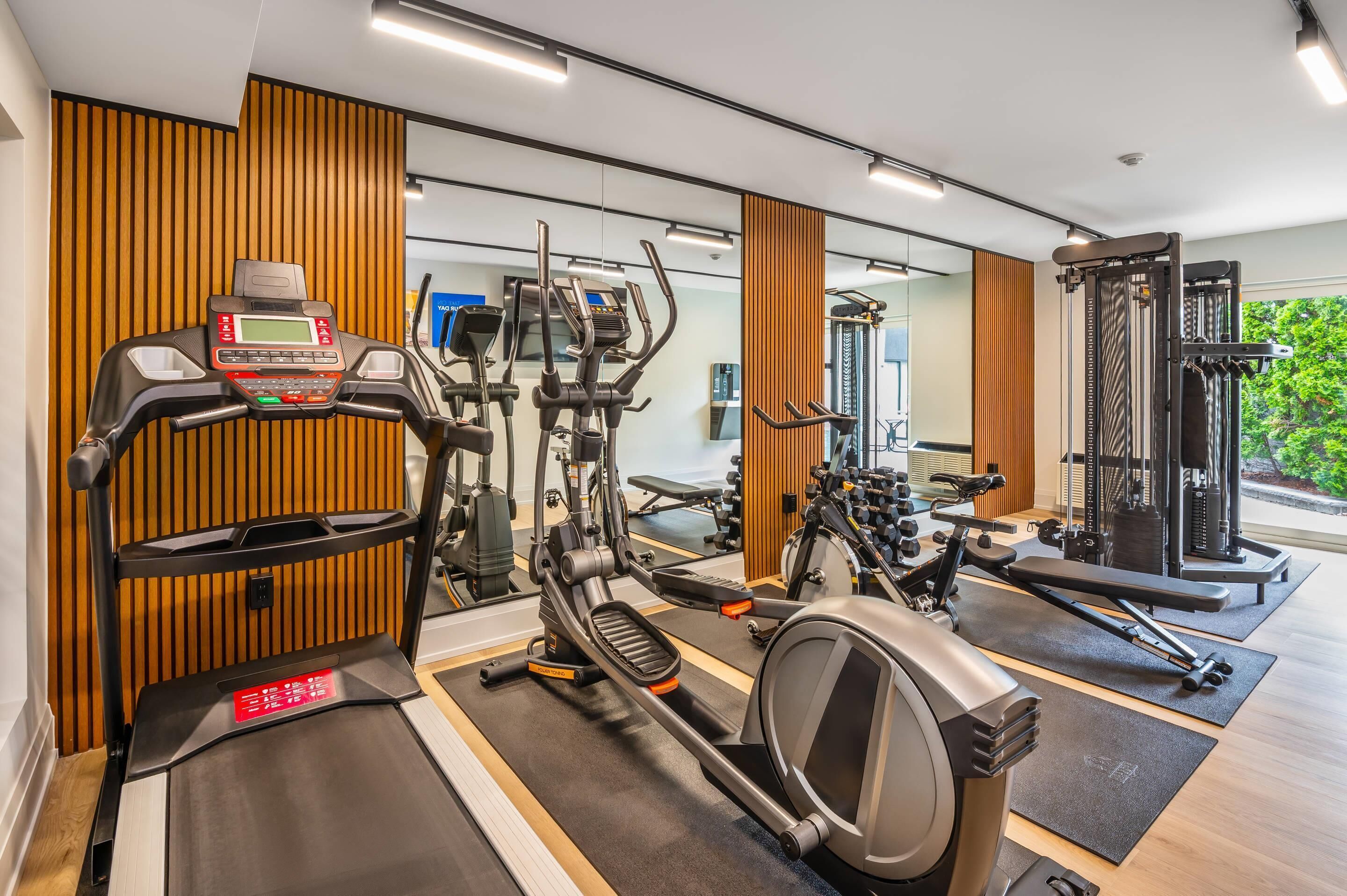 Ein modernes Fitnessstudio mit verschiedenen Trainingsgeräten, Holzpaneelen und einem großen Spiegel, der die Ausrüstung reflektiert.