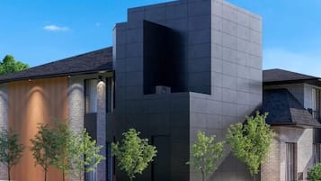 Un edificio moderno con una fachada oscura destacada, una entrada amplia y abierta, y un área verde con árboles al frente.