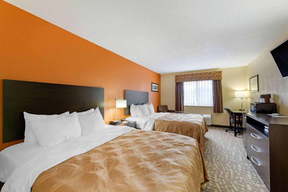 A hotel room with two beds, a desk, a chair, a dresser, and a television.