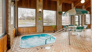 An indoor pool area with a hot tub, wooden beams, and a seating area with tables and chairs. - Quality Inn Wooster (Wooster)