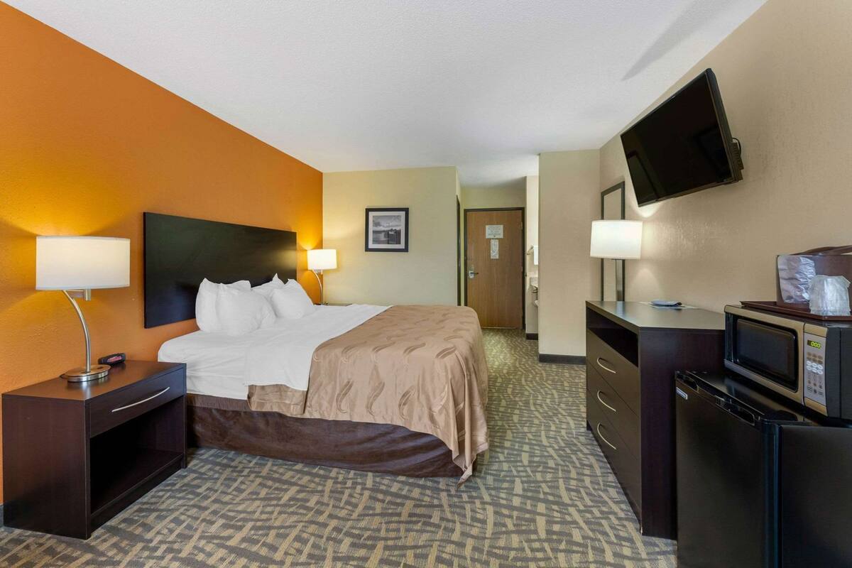 A hotel room with a bed, bedside tables, a TV, a microwave, and a refrigerator.