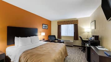 Quarto de hotel com cama, escrivaninha, cadeira e televisão.