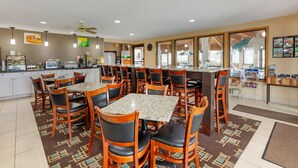 A spacious dining area with multiple tables and chairs, a kitchen in the background, and a large window providing natural light. - Quality Inn Wooster (Wooster)