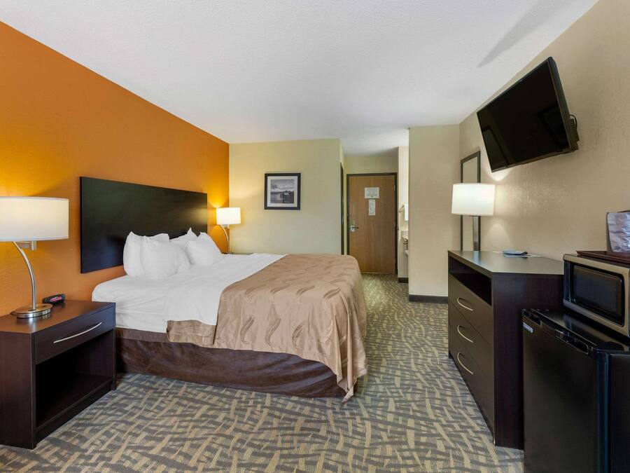 Une chambre d’hôtel équipée d’un lit, de lampes de chevet, d’un téléviseur à écran plat, d’un four à micro-ondes et d’un réfrigérateur.