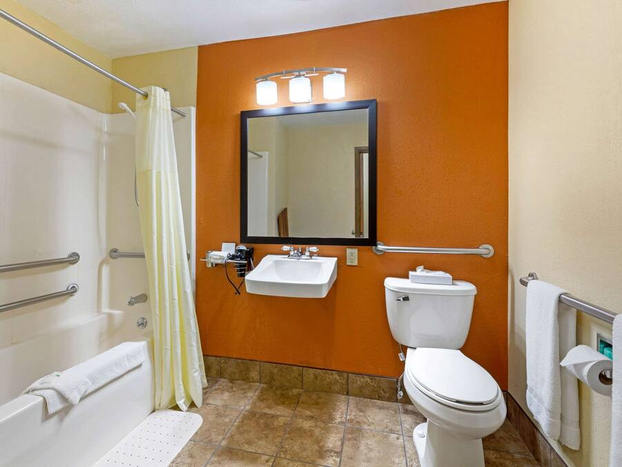 A bathroom with a shower, toilet, sink, and a mirror with lights.