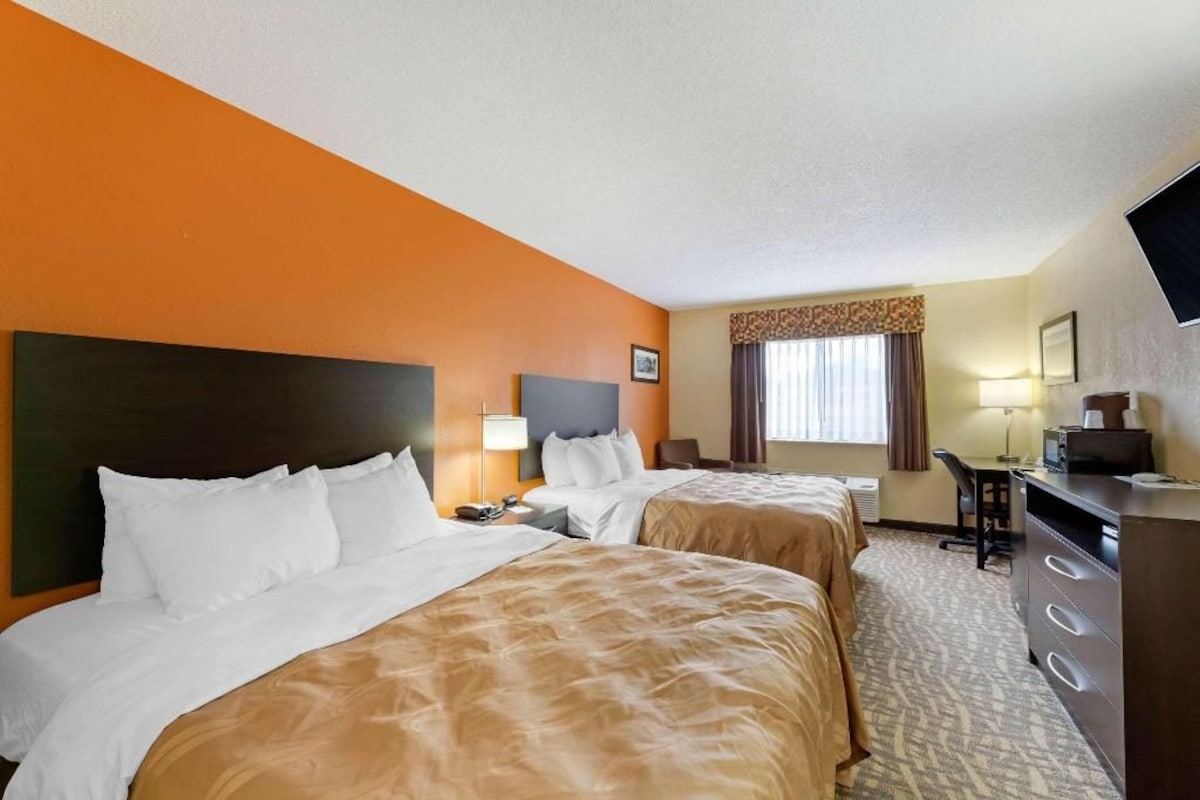 A hotel room with two beds, a desk, a chair, and a television.