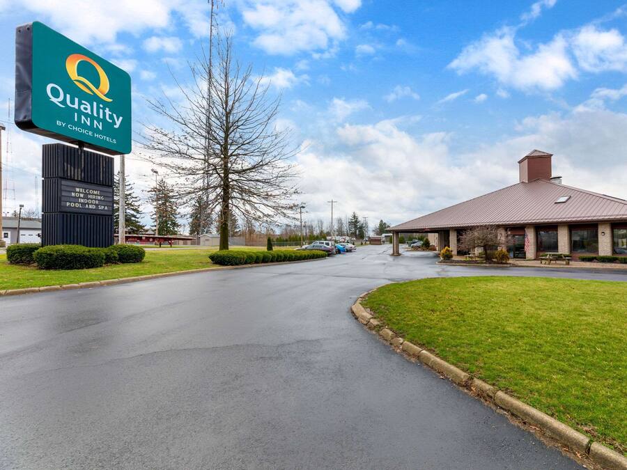 A Quality Inn by Choice Hotels with a large sign, a building with a red roof, and a parking lot.