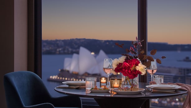 Mesa posta para dois com vista para a paisagem urbana e para a água ao fundo.