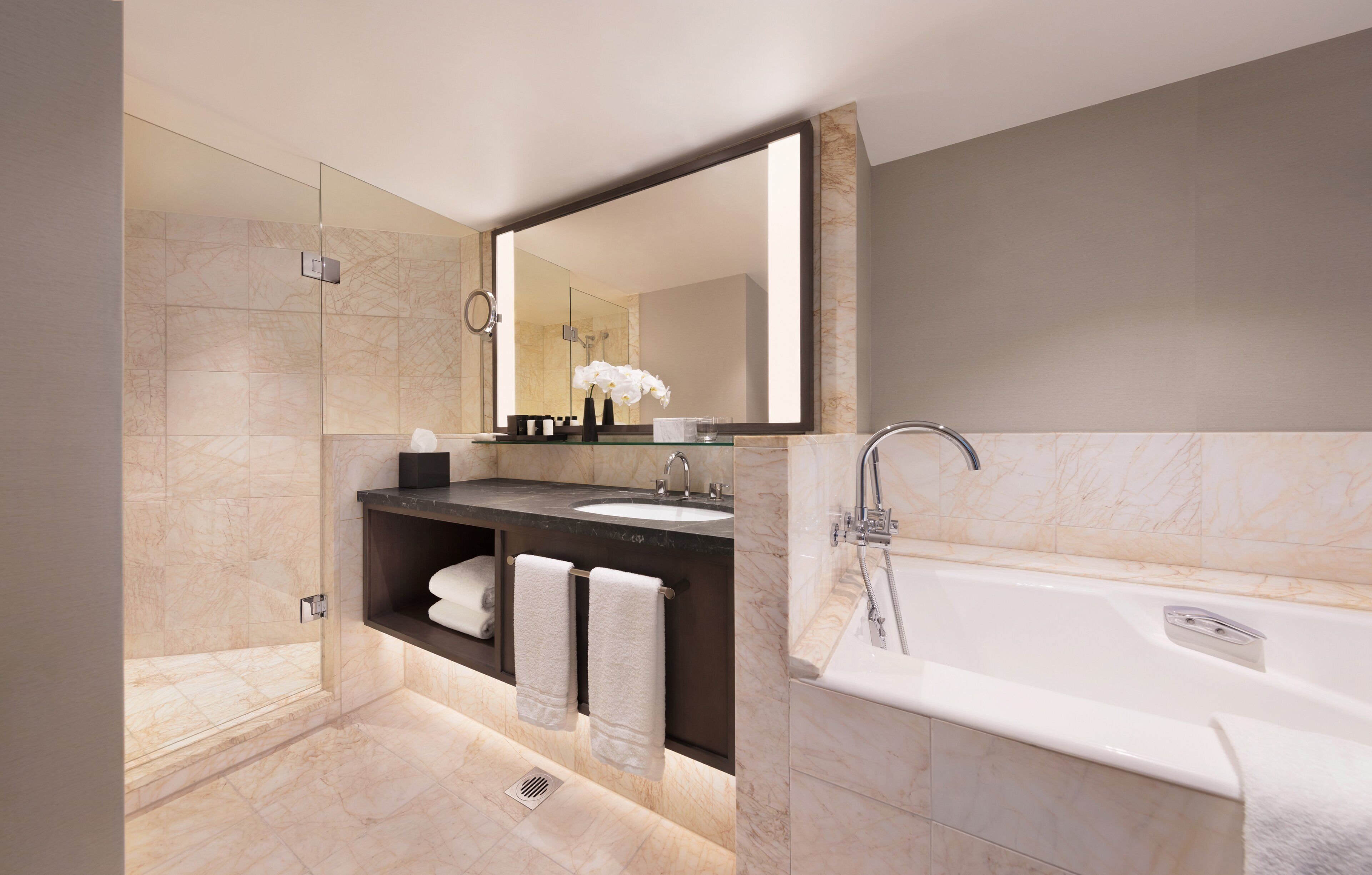 A modern bathroom with a glass-enclosed shower, a large mirror, a bathtub, and a vanity with a sink and towel rack.
