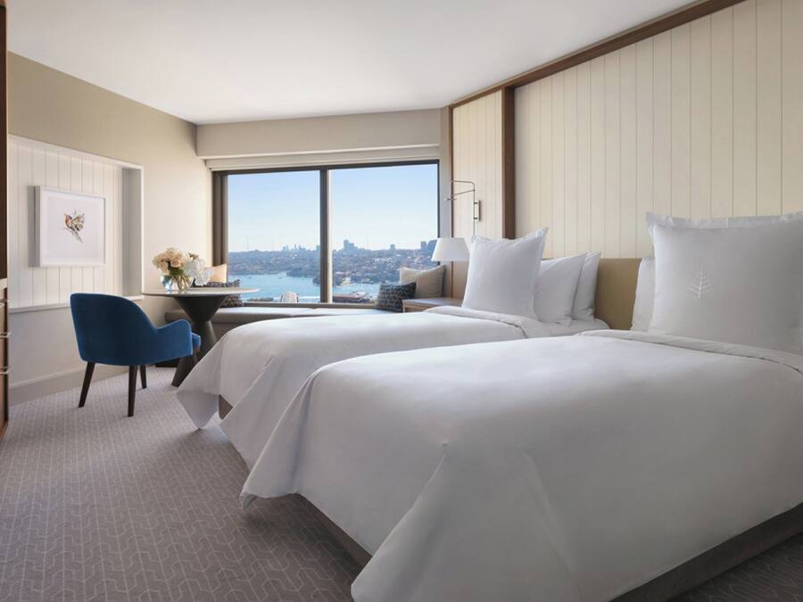A hotel room with two beds, a desk, and a view of the city.