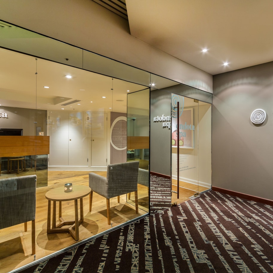 A modern spa area with glass walls, comfortable seating, and a carpeted floor.