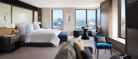 A modern hotel room with a large bed, a sofa, a small table, and a view of a cityscape.