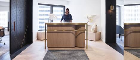 Un área de recepción moderna con un escritorio de madera, un ventanal grande y una escultura decorativa de un pájaro.