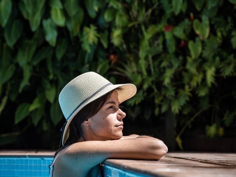 Una persona relajándose junto a una piscina, con un seto verde exuberante al fondo.