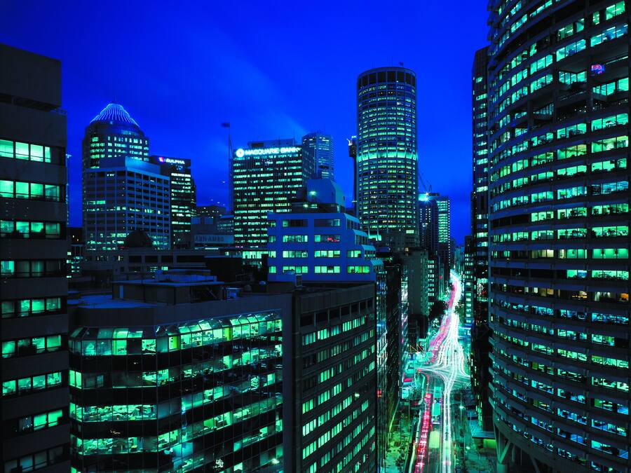 Paisagem urbana noturna com edifícios iluminados e uma rua movimentada.