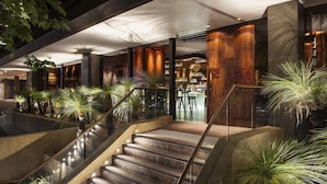 Um hall de hotel moderno com escadas, plantas em vasos e um espaço de bar.