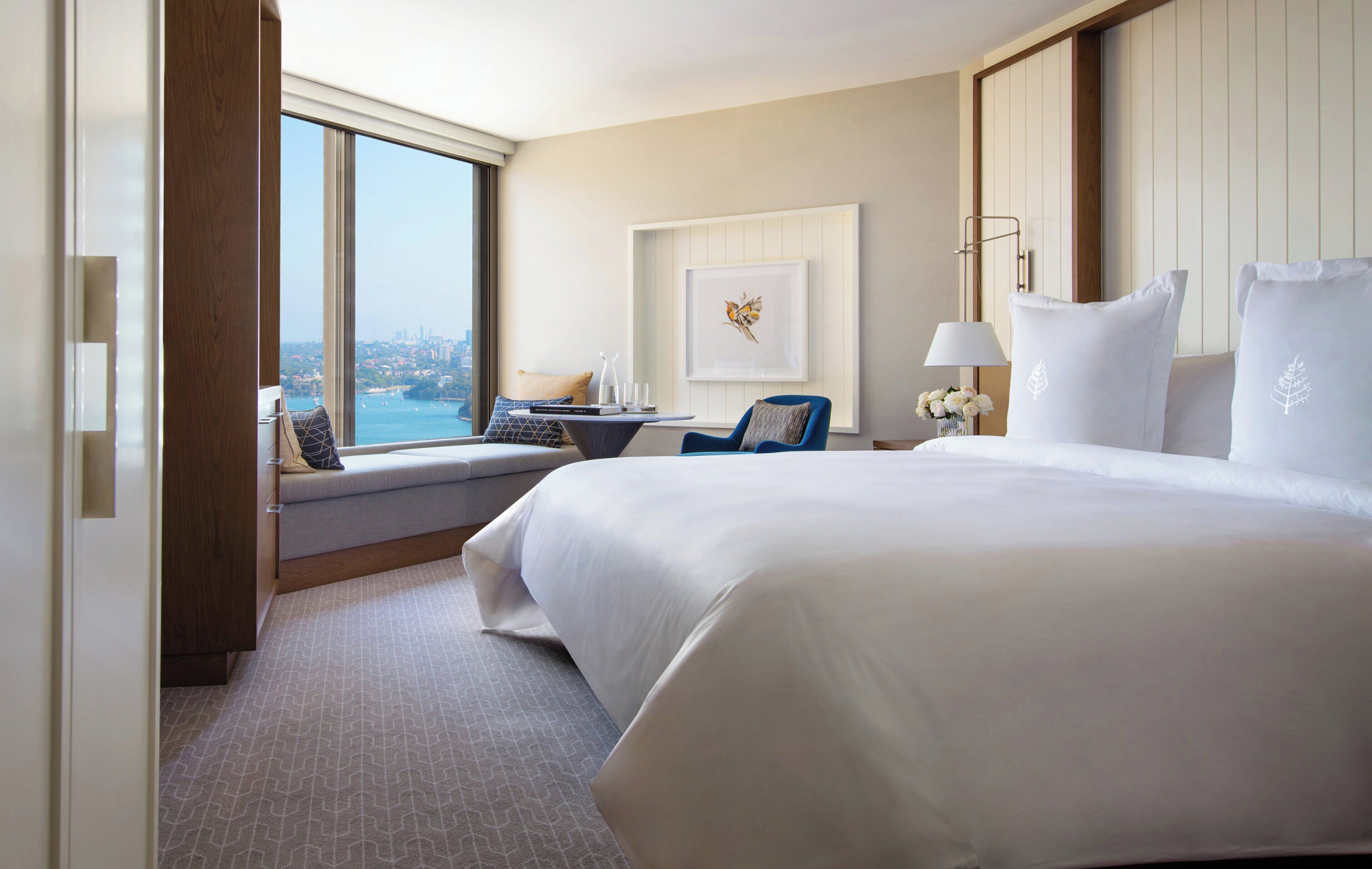 Habitación de hotel con una cama grande, un escritorio con silla, vista a la ciudad y un cuadro en la pared.