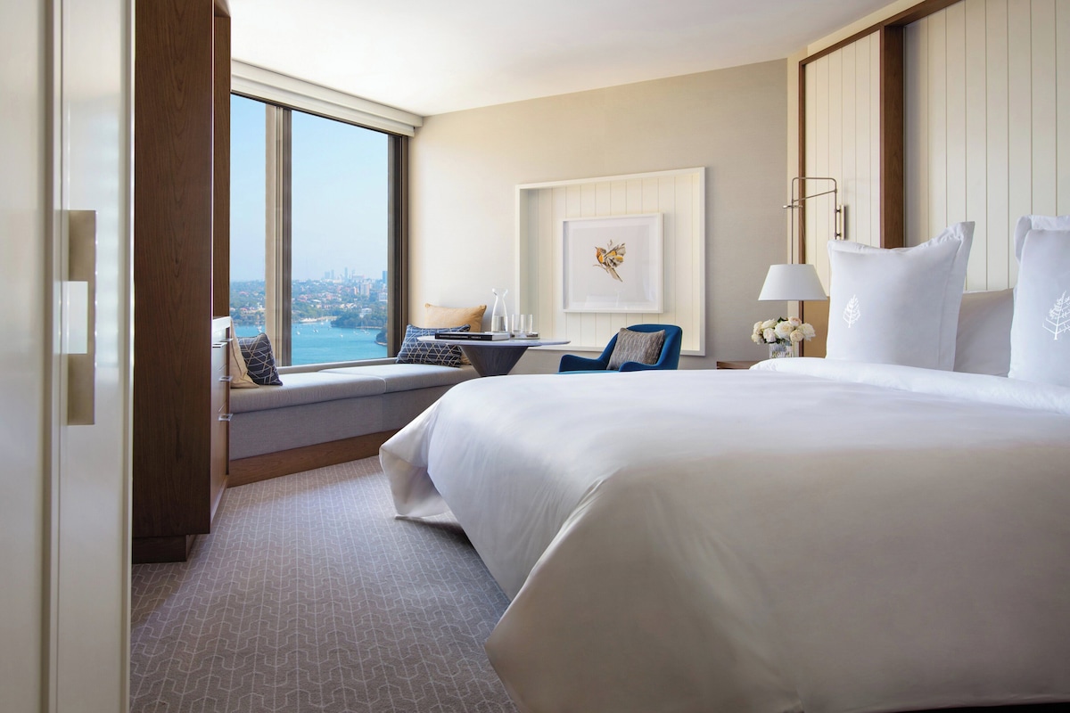 Habitación de hotel con una cama grande, un escritorio con silla, vista a la ciudad y un cuadro en la pared.