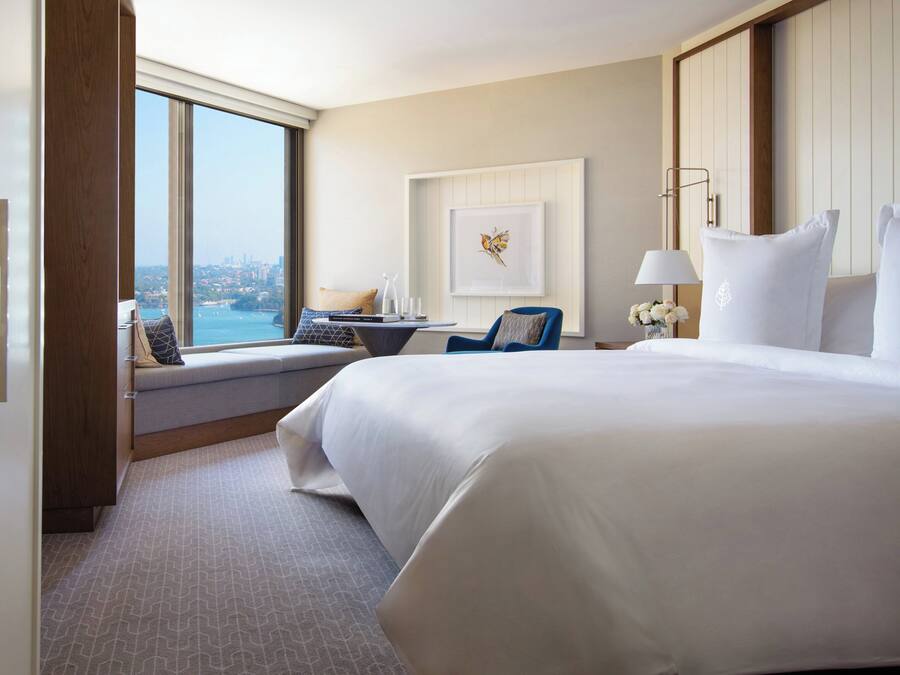 Habitación de hotel con una cama grande, un escritorio con silla, vista a la ciudad y un cuadro en la pared.