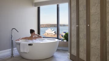 A large freestanding bathtub with a view of a coastal cityscape through a large window.