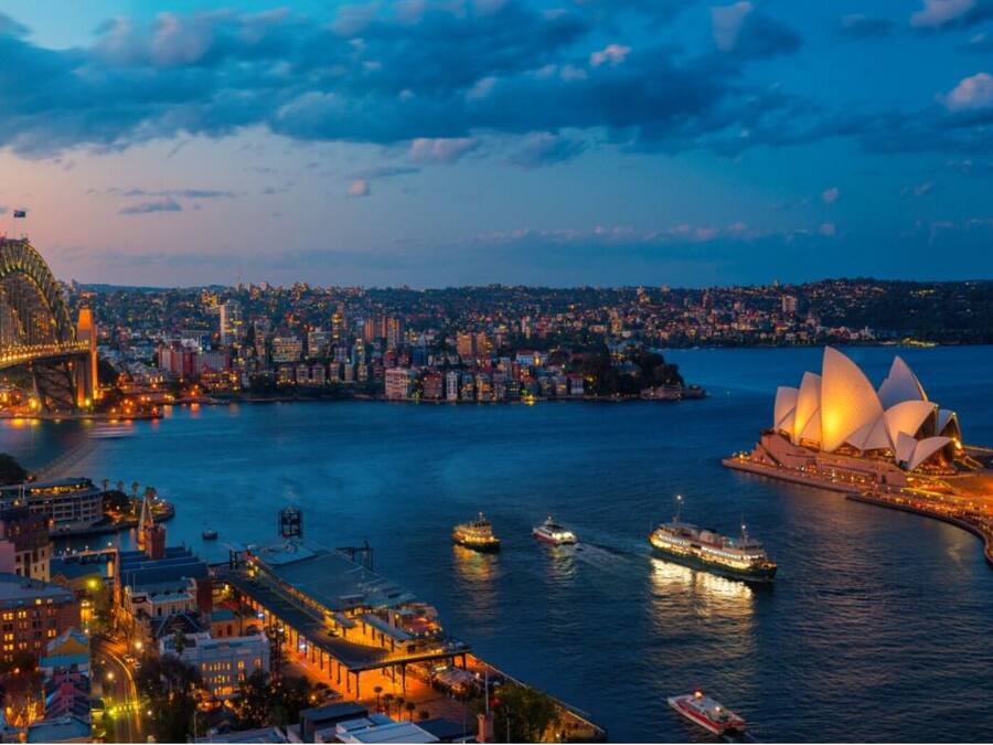 A cityscape with a prominent bridge and a large opera house by the waterfront.