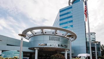 A modern hotel with a curved entrance, a prominent American flag, and a sign reading 'RADISSON PLAZA HOTEL & SUITES'.