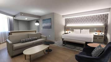 Une chambre d’hôtel moderne avec un canapé, une petite table ronde, un fauteuil sombre, un grand lit avec une tête de lit, des tables de chevet avec des lampes et un mur à motifs.