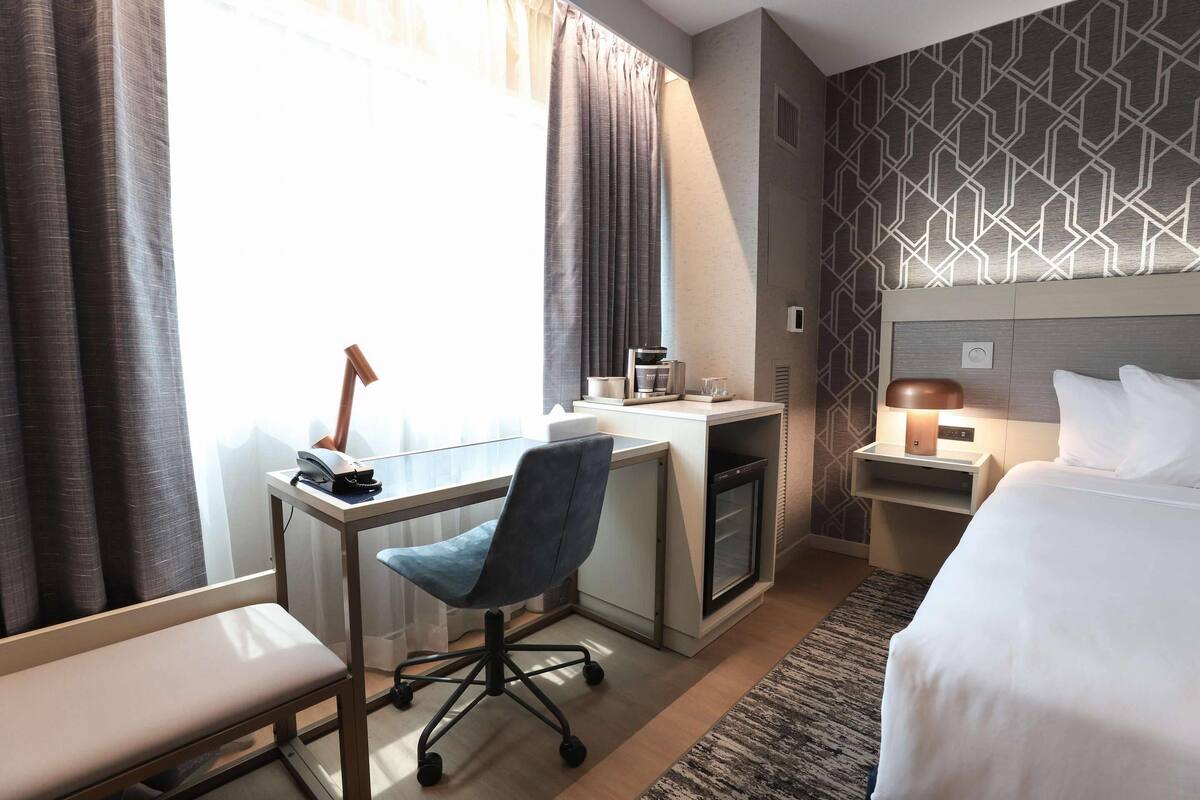 Una habitación de hotel con cama, escritorio, silla y una pequeña kitchenette.