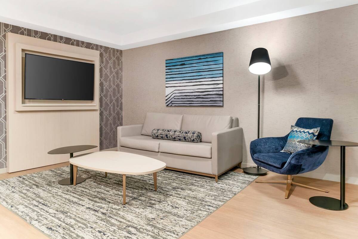 Una sala de estar moderna con un sofá, un sillón azul, una mesa de centro, un televisor y una lámpara de pie.