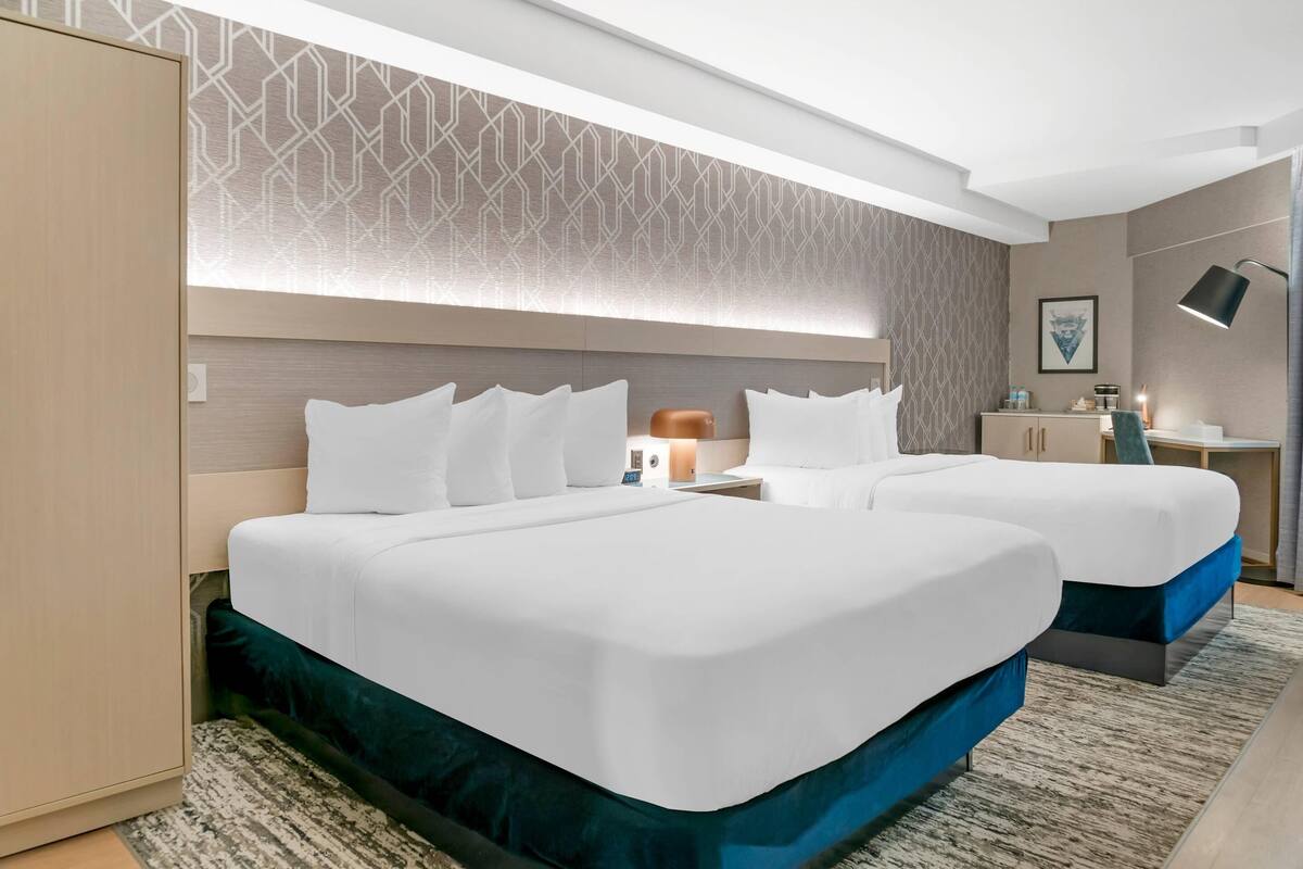 Habitación de hotel con dos camas, un armario, un escritorio y una mesita de noche.