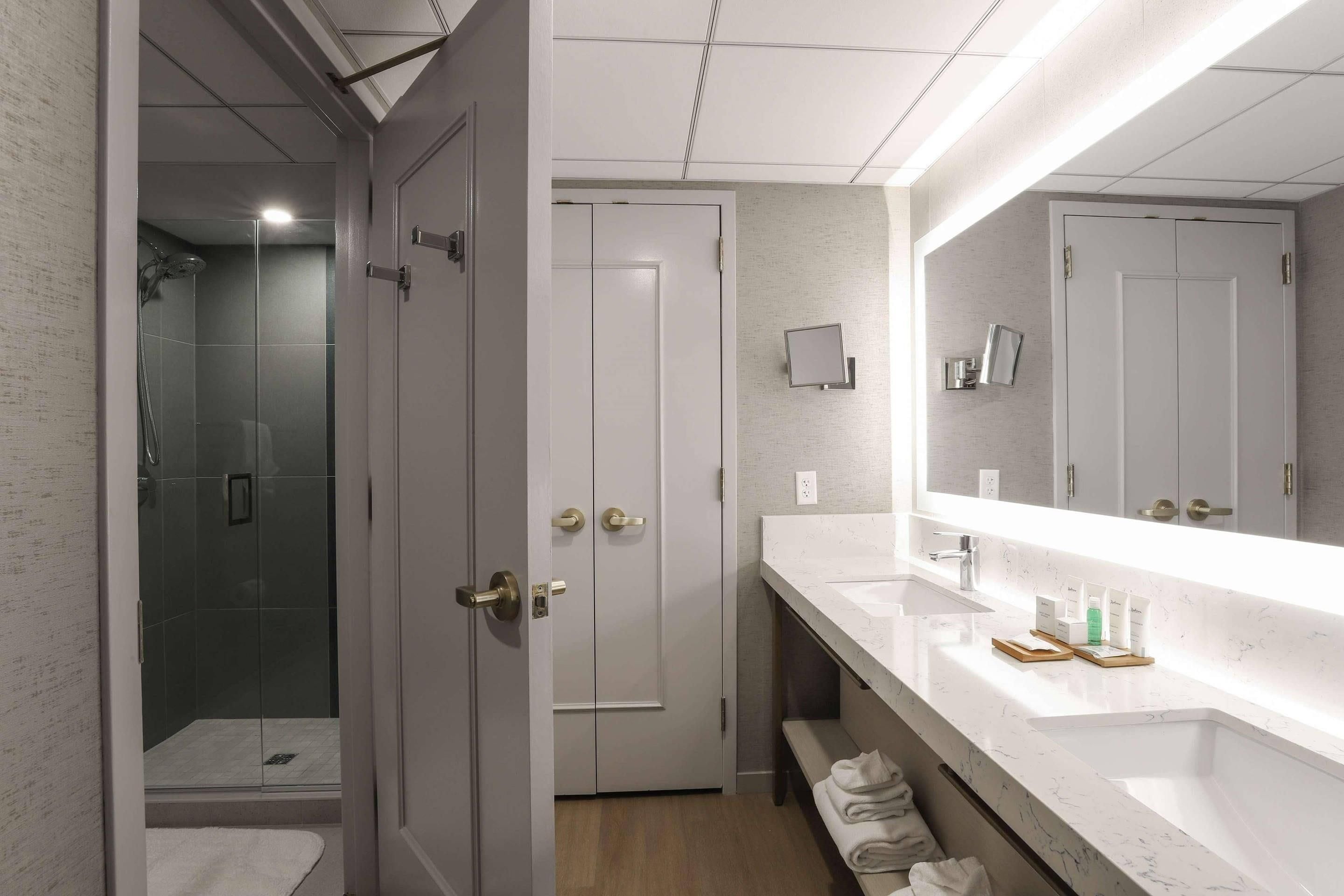 A modern bathroom with a large mirror, a shower, and a vanity with a sink and towel rack.
